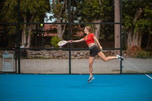 woman in red tank top and black shorts holding tennis racket